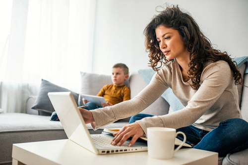 Photo credit:Smiling mom working at home with her child on the sofa while writing an email. Young woman working from home, while in quarantine isolation during the Covid-19 health crisis © Dragana Gordic. Shutterstock.com